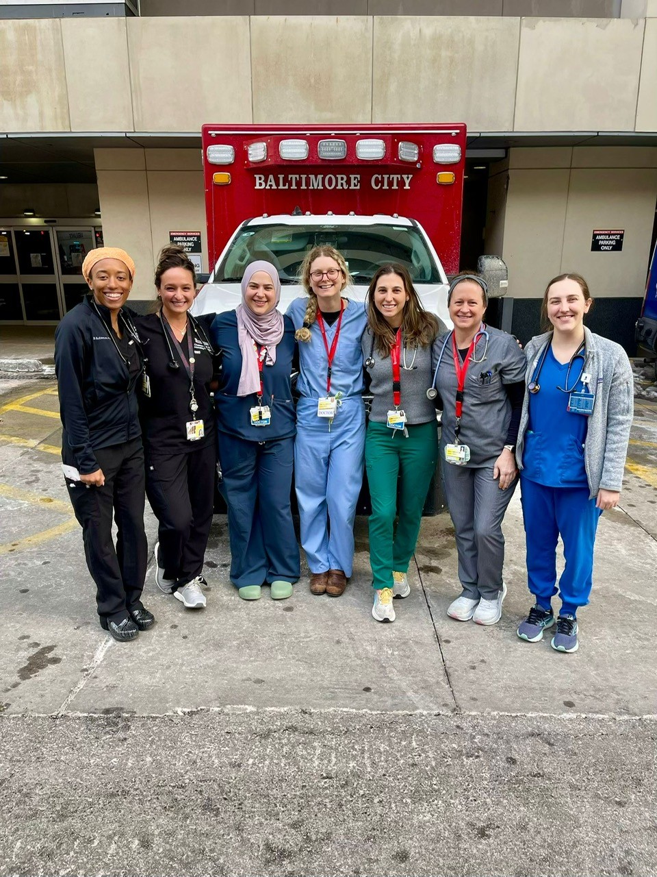 Group of seven female physicians pose in front of a Baltimore City ambulance