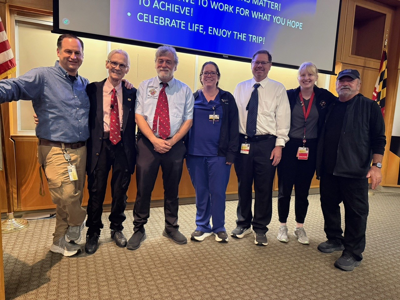 Mixed group of seven physicians pose in front of a lecture room.