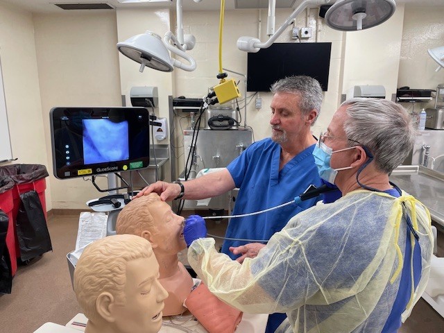Two male physicians perform a procedure focused on the nasal passages of a male model.